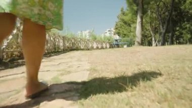 Kamera, çit boyunca bir parkta yürüyen genç bir kadının ayaklarını takip ediyor..