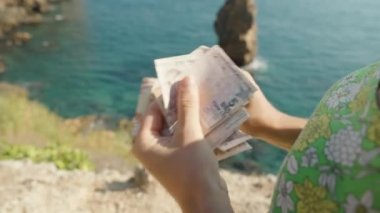 Yeşil elbiseli genç bir kadın deniz ve kayaların arkasında para sayıyor. Yakın plan.