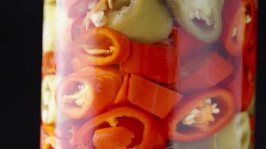 Bir kavanoz turşulu kırmızı biber siyah arka planda yakın planda döner.