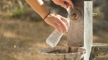 Ormanda içme suyu muslukları olan bir tezgah, genç bir kadın gelir ve şişeyi doldurur. Kapat.
