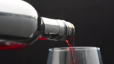 Siyah arka planda bir bardağa kırmızı şarap döküyorum. yakın plan.