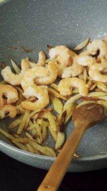 Karidesler kızartma tavasına yağ ve kızarmış soğanla konur, kaşıkla karıştırılır, yakın çekim dikey video..