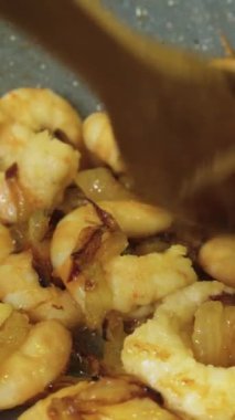 Karidesler kızartma tavasına yağ ve kızarmış soğanla konur, kaşıkla karıştırılır, yakın çekim dikey video..