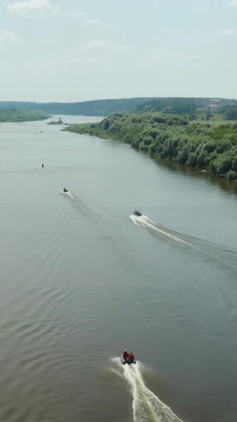ドローンだ 川の上を飛ぶ 田舎の家 ボートは川に沿って航行する 人々は泳いでいる ボートの後ろに飛ぶ垂直ビデオ — ストック動画