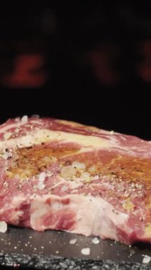 Ateşin arka planında dönen bir biftek parçası. Kırmızı biber serpiştirilmiş dikey video.