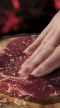 Ahşap tepside biftekler ateşin arka planında. Baharatlarla ovarım. Dikey video.