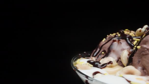 一个装有巧克力冰淇淋球和糖洒水的杯子在黑色背景上旋转 — 图库视频影像