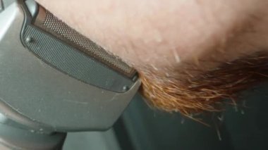 Kızıl sakallı bir adam elektrikli jiletle tıraş olur. Çok geniş bir çerçeve. POV
