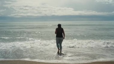 Fırtınalı deniz ve bulutlar, taytlı tombul genç bir kadın denize giriyor..