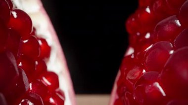 Siyah bir zemin üzerinde kırmızı bir nar dilimlenir, kamera tanelerin içinden geçer, aşırı yakın plan..