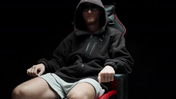 一个戴着黑色眼镜 头戴黑色夹克 坐在游戏椅子上打转的男人 — 图库视频影像