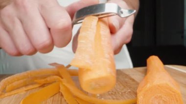 Bir kız sebze soyacağı ile havucun kabuğunu kesiyor, yakın plan..