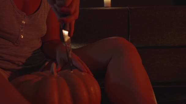 赤い光でキャンドルライトで若い女性は カボチャにナイフを突っ込む — ストック動画