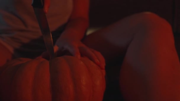 赤い光の夜の若い女性はハロウィーンのカボチャを彫っています クローズアップインモーション — ストック動画