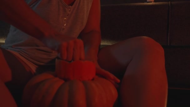 赤いライトでキャンドルライトで若い女性はハロウィーンのカボチャを彫ります コアを引き出す — ストック動画