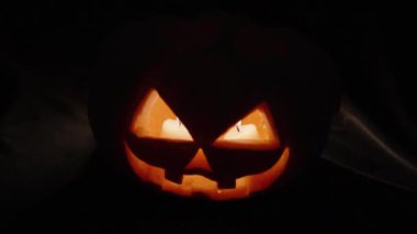 Cadılar Bayramı için bir balkabağı, içinde iki mum yanıyor, içinden su damlıyor. Siyah arkaplanda yakın plan