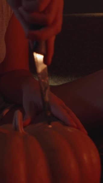 バーティカルビデオ 赤い光でろうそくに照らされた若い女性は カボチャにナイフを挿入します — ストック動画