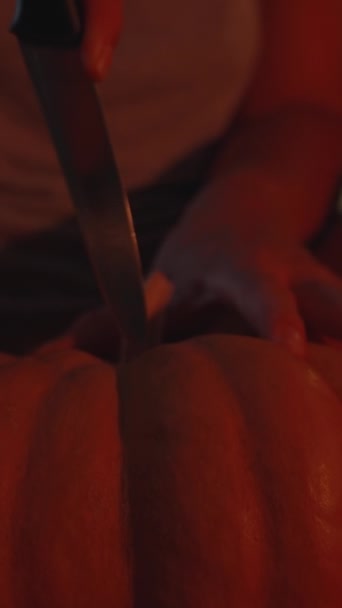 Függőleges Videó Egy Fiatal Tököt Vág Halloweenkor Vörös Fényben Közelkép — Stock videók