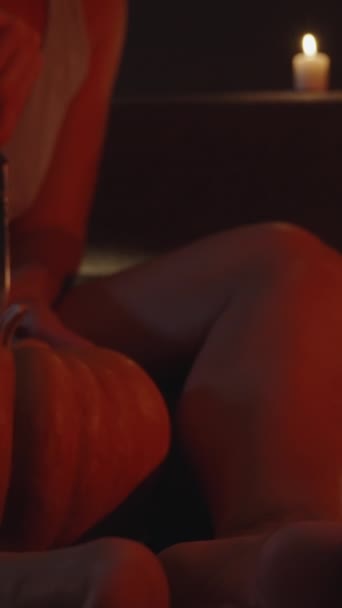 バーティカルビデオ ハロウィーンのためのカボチャを彫る赤いライトのろうそくによって照らされる若い女性 — ストック動画