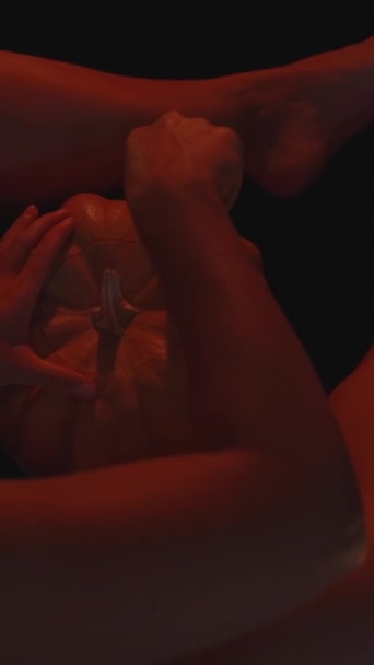 バーティカルビデオ ハロウィーンのカボチャを彫った赤い光でろうそくに照らされた若い女性 内部をスカウトする トップビュー — ストック動画