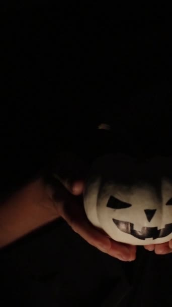 バーティカルビデオ 暗闇から出現する手 ホワイトハロウィーンのカボチャを保持 ボンファイアで照らされた — ストック動画