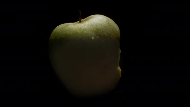 一只绿色被咬的苹果在黑色的背景上旋转 苹果从黑暗中出现在光明中 — 图库视频影像