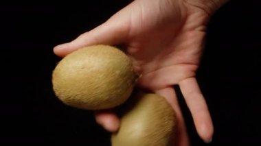 Genç kadın elinde siyah bir arka planda iki kivi tutuyor..