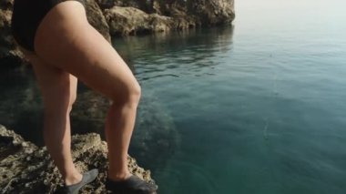 Mayo giymiş genç bir kadın bir kayanın üzerinde duruyor ve elinde ev yapımı bambu oltasıyla denizde balık tutuyor. Balıkçı oltasını sudan çıkardı..