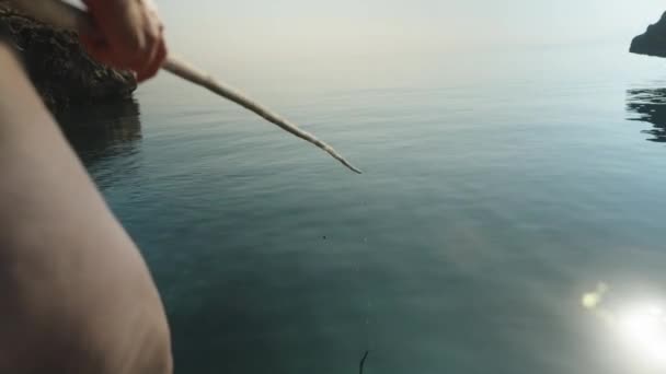 水着の若い女性は自家製の竹釣り棒で海で釣りをしている 水ははっきりしている フロートは沈んでおり 彼女は釣り棒を取り出します — ストック動画