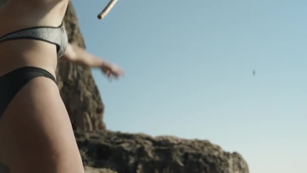 一个穿着泳衣的年轻女子在海里把钓竿扔进了水里 悬崖峭壁的边缘 — 图库视频影像