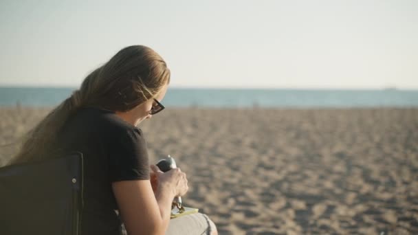 Μια Νεαρή Γυναίκα Κάθεται Μια Καρέκλα Στην Άμμο Στο Βάθος — Αρχείο Βίντεο