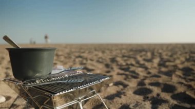 Deniz kenarında güneşli bir hava. Piknik, kumda barbekü standı.