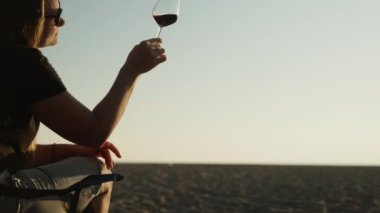 Sahilde romantik bir randevu, genç bir kadın bir bardak şarapla gün batımını izliyor. Yakındaki ızgarada bir ateş yanıyor..