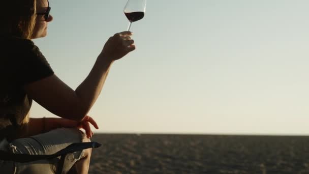 一位年轻女子在海边的浪漫约会中 透过一杯葡萄酒望着夕阳 附近的烤架上着火了 — 图库视频影像