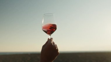 Deniz kıyısında romantik bir randevu, genç bir kadın kadehte şarap döndürür ve gün batımını seyreder. Yakın plan..