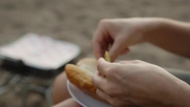 Plajda piknik, bir kız sosisli ekmeğine turşu ve domates koyar..