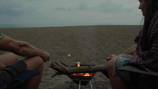 トワイライト 若い女性と私は海でビーチでボンファイアでマシュマロを揚げています — ストック動画