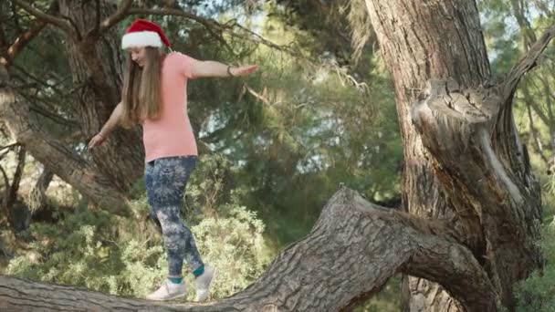 Een Jonge Vrouw Met Een Kerstmuts Loopt Langs Stam Van — Stockvideo