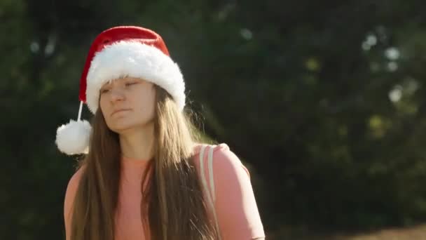Een Jonge Vrouw Met Een Rode Kerstmuts Loopt Tegen Achtergrond — Stockvideo