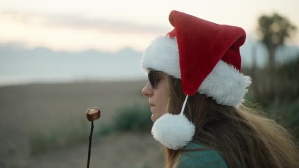 Молода Жінка Червоному Капелюсі Санта Їсть Смажені Зефіри Пляжі Біля — стокове відео