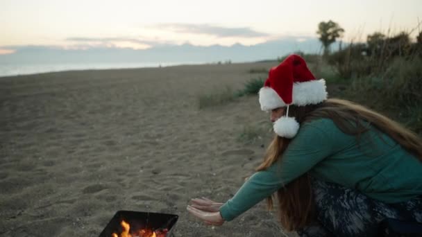 Молода Жінка Пляжі Червоному Капелюсі Санта Зігріваючи Руки Біля Вогню — стокове відео