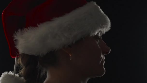 一个戴着圣诞帽 背景是黑色的年轻女子 扭动着头 特写镜头 — 图库视频影像