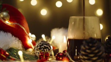 Işıklardan oluşan bir çelengin arkasına sıcak çikolata döküyorum. Mumlar ve dekorasyonlarla dolu bir Noel masası. Yavaş çekim.