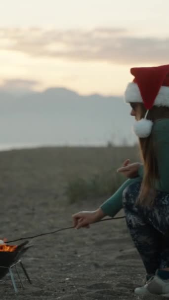 Вертикальне Відео Молода Жінка Червоному Капелюсі Санта Смажить Зефір Пляжі — стокове відео