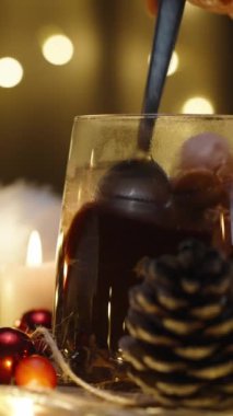 Dikey video. Kakaonun içinde marşmelov karıştırıyorum, arka planda ışıklardan oluşan bir çelenk. Mumlar ve dekorasyonlarla dolu bir Noel masası. Yavaş çekim.