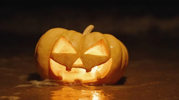 stock image Halloween pumpkin on the seashore, a wave covers it and extinguishes the candles inside, close-up