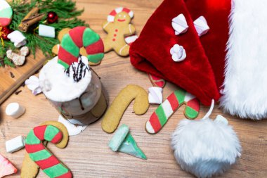 Bir fincan krem şantili sıcak çikolatada zencefilli şeker çubuğu, Noel içeceği. Masanın üstünde Noel Baba 'nın şapkası var. Şekerlemeler her yere saçılmış..