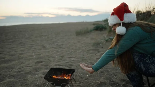 Young Woman Beach Red Santa Hat Warming Her Hands Fire — Stock Photo, Image