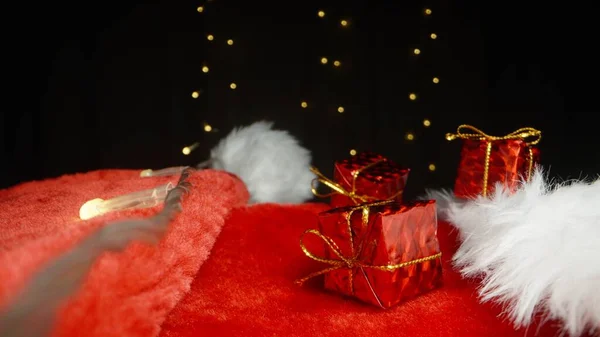 三个红色的小礼品盒放在圣诞老人的帽子上 旁边是一个闪烁着光芒的花环 后续行动 — 图库照片