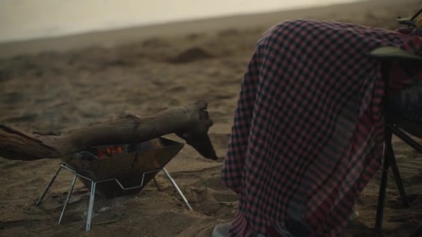 一个年轻的女人在海滨篝火边被毛毯覆盖着 惊讶地看着电话 日落时分 — 图库视频影像
